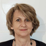 Frau Wurziger-Keltsch mit kurzem, dunkelblondem Haar, trägt schwarze Oberbekleidung und eine Kette mit großen, unregelmäßigen Anhängern