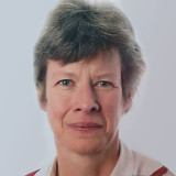 Frau Sprügel mit kurzem, graubraunem Haar, trägt ein hellrosa Hemd mit Kragen vor hellem Hintergrun